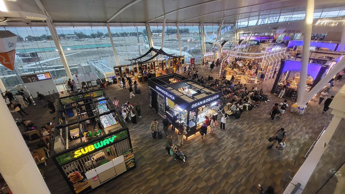 Busy departures concourse at Phuket International Airport with food kiosks and seated passengers — Thailand travel costs start at the transfer desk