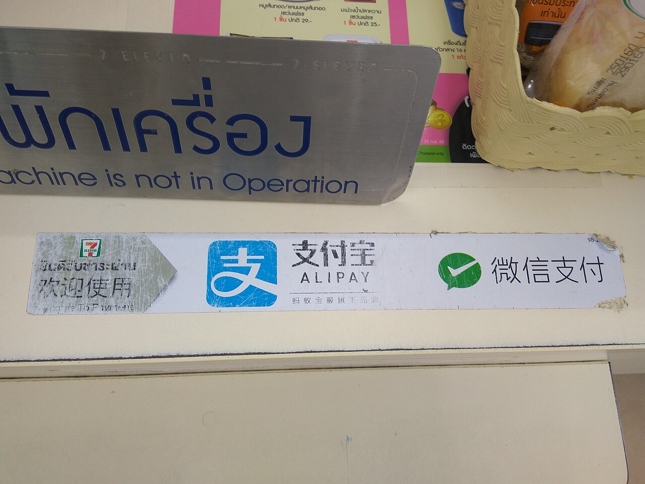 7-Eleven Thailand checkout counter with Alipay and WeChat Pay stickers and Thai promotional price cards showing 25 and 29 baht - paying for cheap travel Thailand purchases