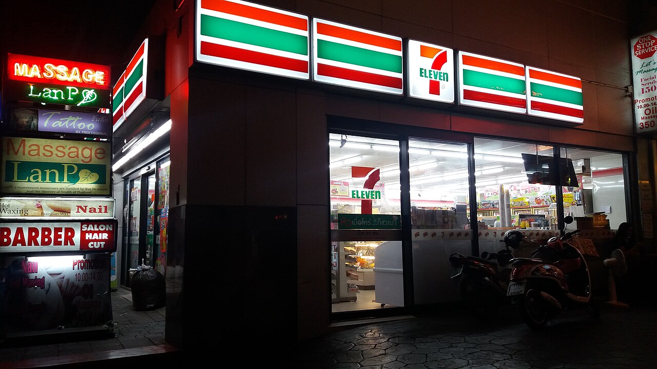 A 7-Eleven store lit up at night on Sukhumvit Road in Bangkok, next to a massage shop - the cheapest everyday prices for cheap travel Thailand