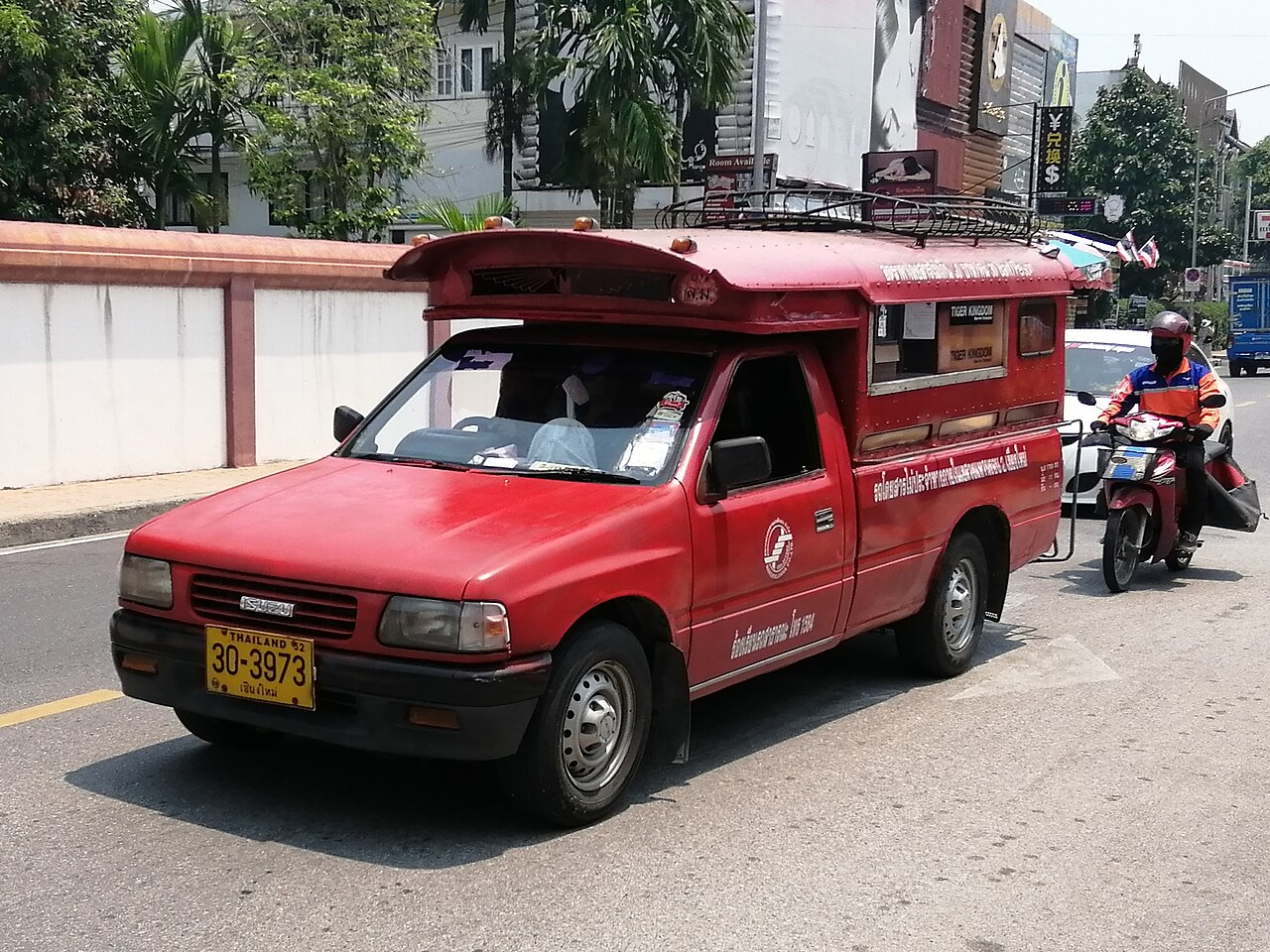 A red songthaew shared taxi truck with Chiang Mai plates on a city street, the 30 to 40 baht ride that keeps Thailand travel costs down between the airport and the Old City
