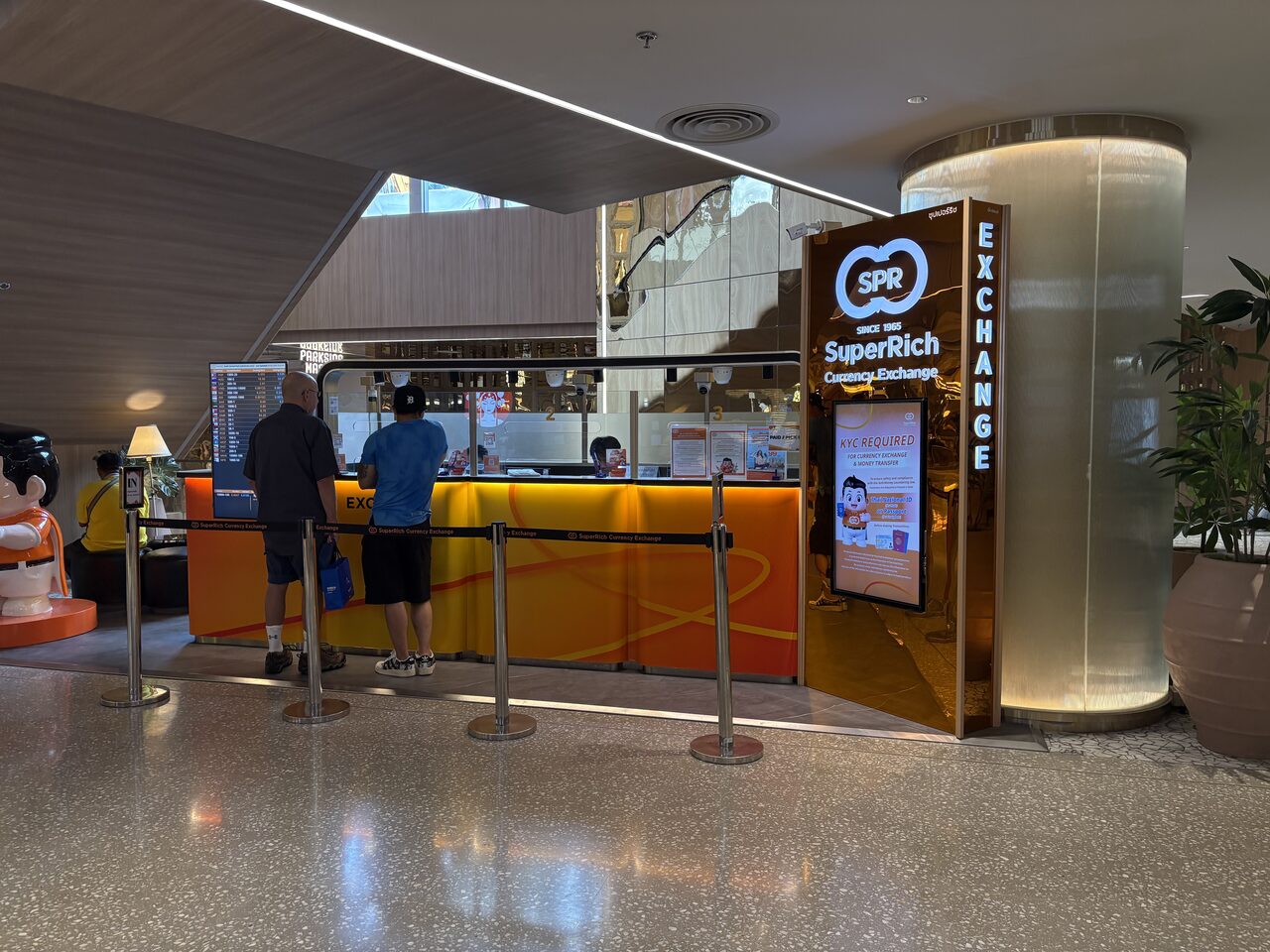 Travellers at a SuperRich currency exchange counter in Bangkok with the rate board on the left, the money exchange Thailand setup where note denomination changes the Thai baht exchange rate