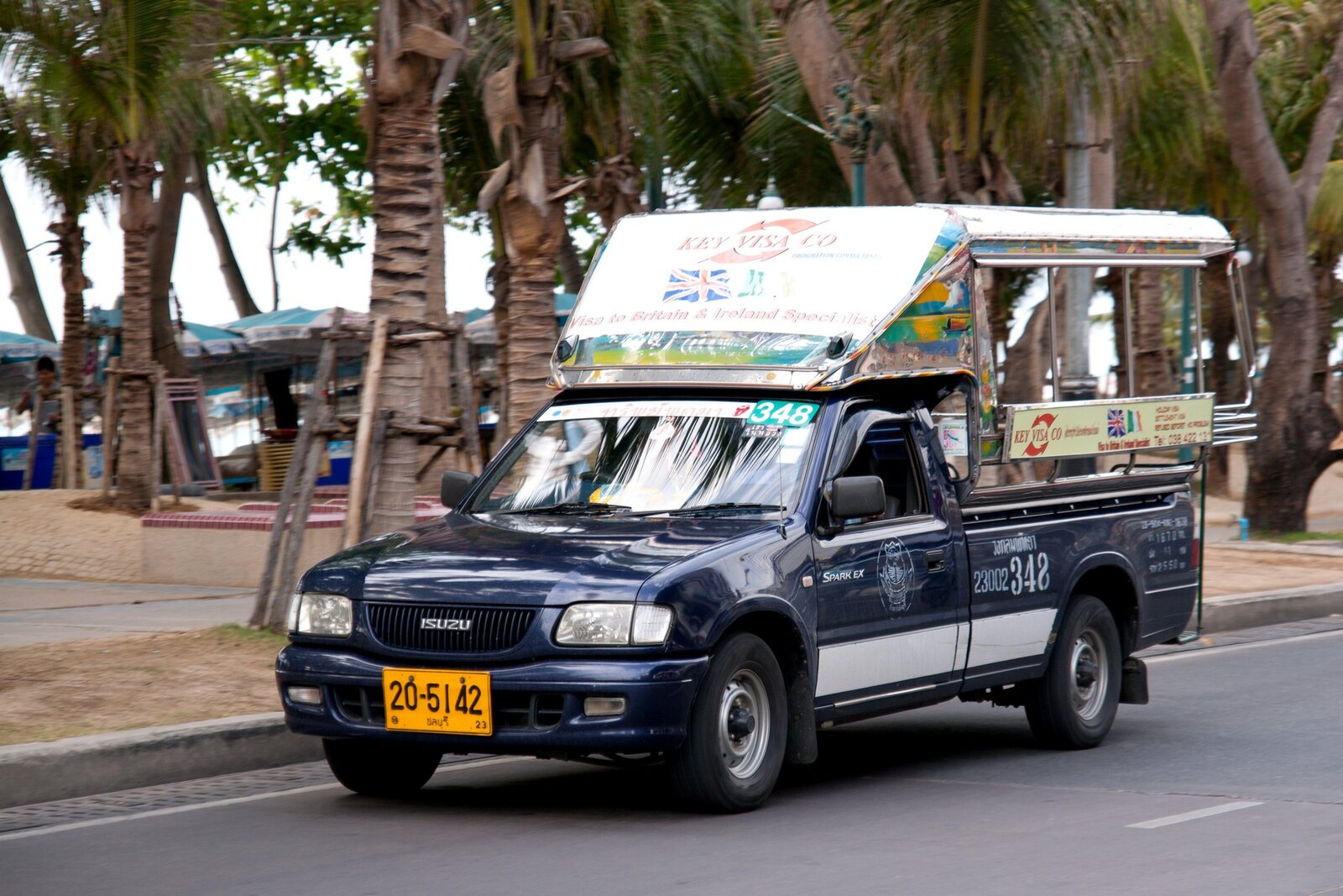 A blue route-numbered songthaew baht bus driving along Beach Road in Pattaya past palm trees, the 15 baht shared service that keeps Thailand travel costs down for short hops