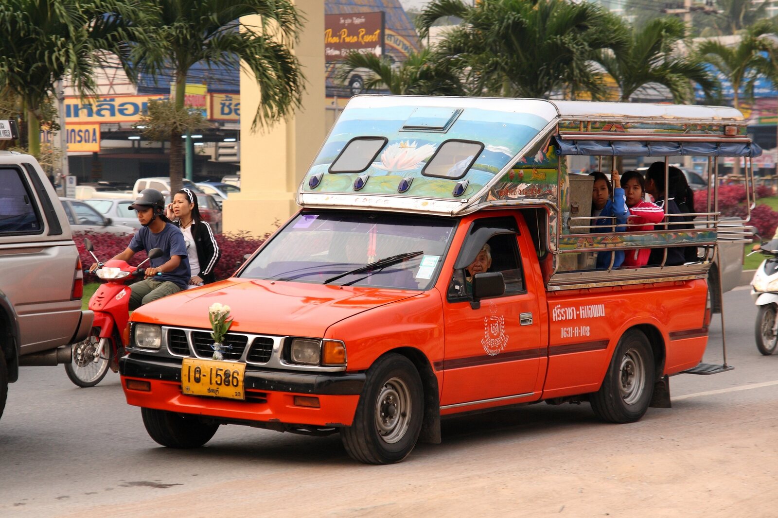 An orange intercity songthaew on Sukhumvit Road near Pattaya carrying seated passengers on the Sriracha to Naklua shared route, where Thailand travel costs run 20 to 40 baht by distance