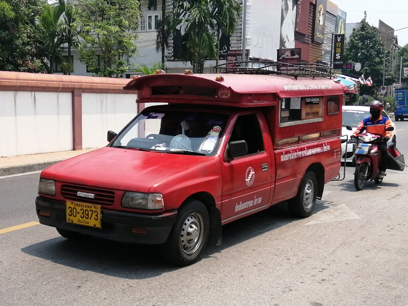 A red songthaew shared taxi truck on a Chiang Mai street with a yellow Chiang Mai licence plate, the 30-baht ride at the centre of cheap travel Thailand transport costs