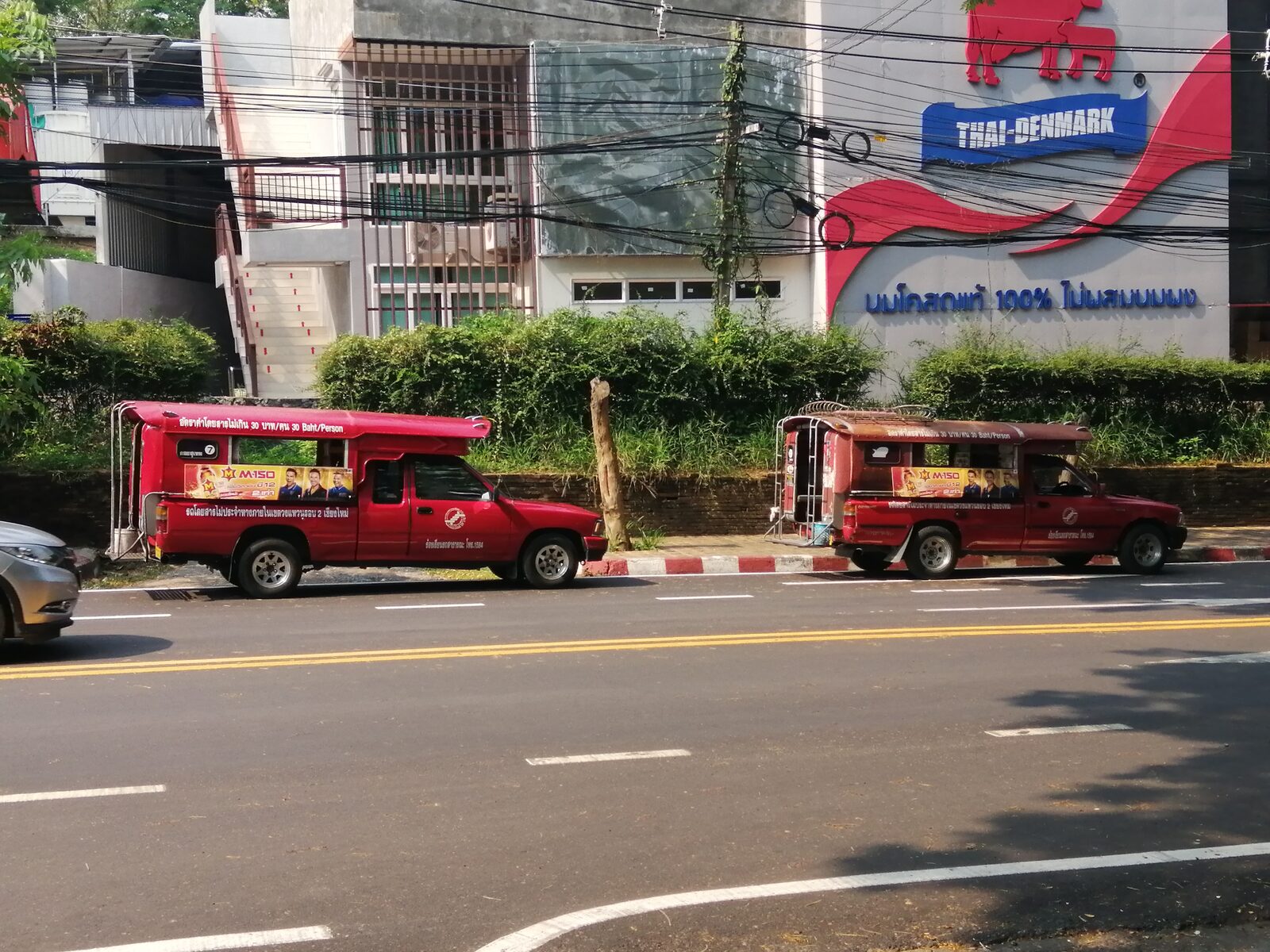 Two Chiang Mai red songthaews parked at the kerb with the official 30 Baht per Person fare sign printed along the roof, the posted cap behind Thailand travel costs in Chiang Mai
