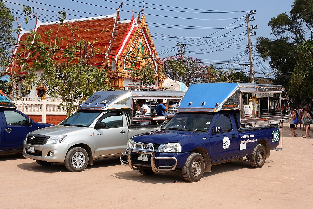 Numbered shared songthaew pickup taxis waiting by the temple in Na Baan village on Koh Larn, Thailand, charging 20 to 50 baht a person to the beaches in this budget travel guide