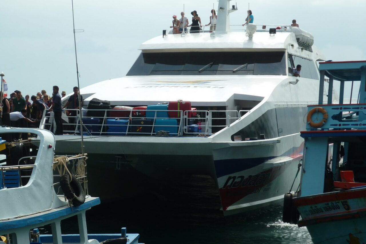 A Lomprayah high-speed catamaran berthed at a Thai pier with passengers and luggage stacked on the bow deck, the boat used for Thailand budget travel from Chumphon to Koh Tao