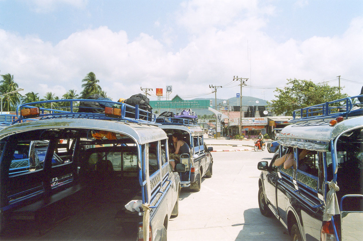Songthaew pickup taxis with roof racks queueing for ferry passengers at Thong Sala pier on Koh Phangan, the shared ride used for cheap travel Thailand transfers to Haad Rin
