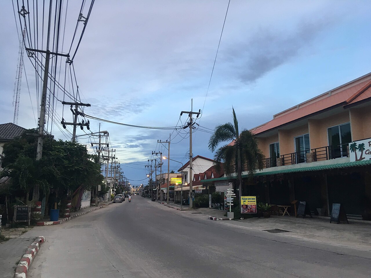 The main street through Thong Sala town on Koh Phangan at dusk, lined with shophouse restaurants where Thailand travel costs stay near mainland prices