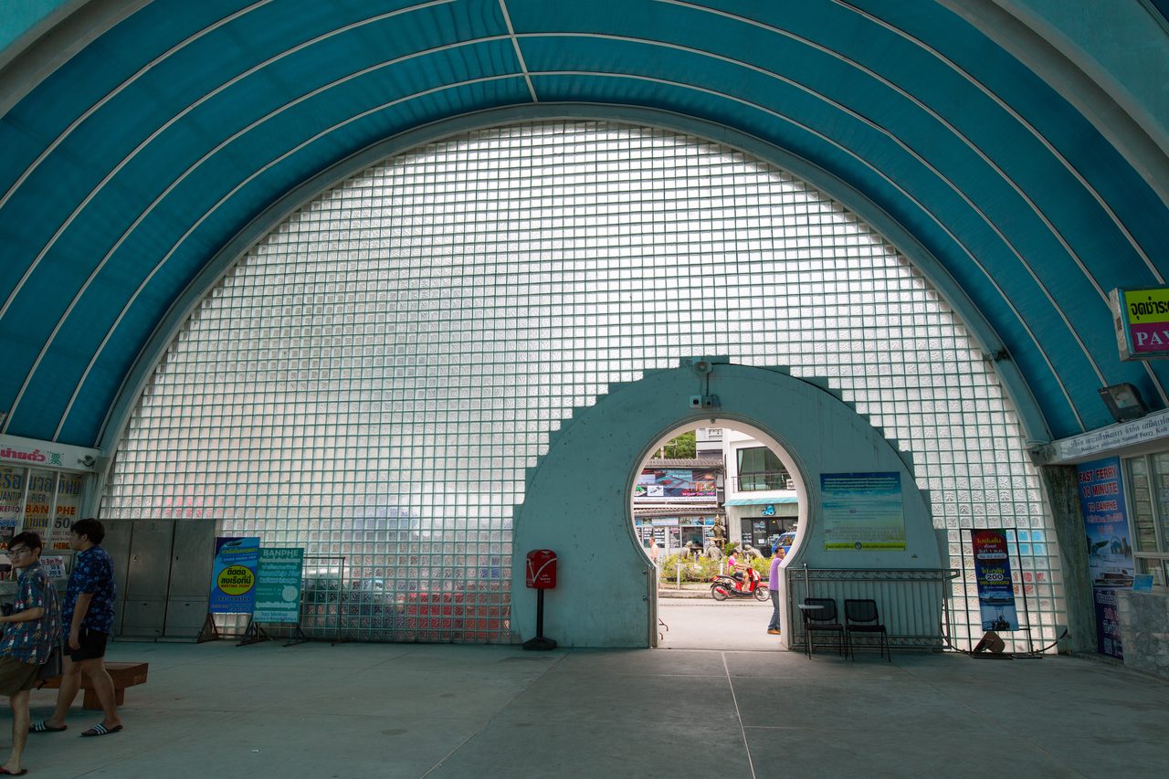 The ticket hall at Ban Phe pier in Rayong with operator signboards, where Thailand travel costs for Koh Samet ferry and speedboat tickets are posted