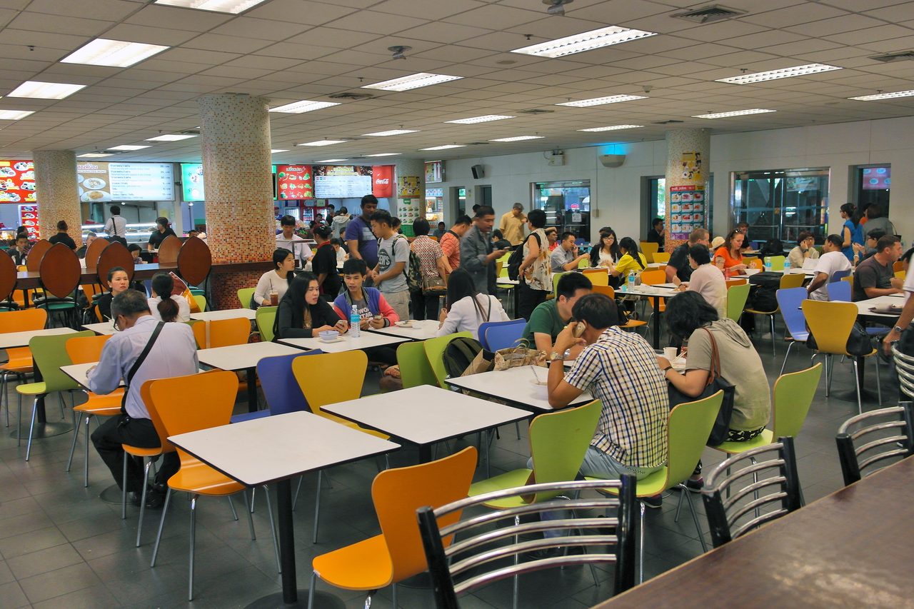 Canteen-style food court inside Suvarnabhumi Airport in Bangkok with stall menu boards and communal tables, where cheap food in Bangkok airport terminals is sold at street prices